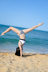Back side view of acrobatic woman doing exercises on sandy beach sunny background outdoors