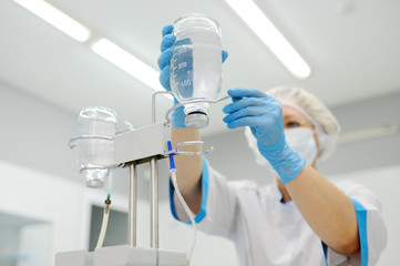 Doctor woman in medical mask and sterile gloves preparing a patient for surgery. Dropper into a vein close-up on a background of the surgical operational