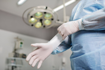 Doctor puts on latex gloves on the background of the surgical lamp. A surgeon preparing for surgery