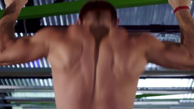 Caucasian sportsman doing pull ups at the gym. Strong male athlete hanging backwards to the camera. Muscular man with bare torso lifting his body up on the bar