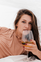 Portrait of attractive woman relaxing in bed enjoying wine on blue sky sea outdoors background. Enjoyment luxury