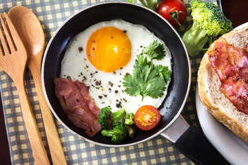 Breakfast with fried egg and bacon in dark pan on the table
