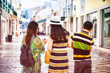 Trois touristes de dos, regardant un téléphone portable dans une rue de la ville de Faro, région d'Algarve, Portugal 