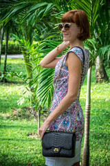 Outdoor fashion portrait of glamour sensual young stylish lady in sunglasses with luxury handmade snakeskin python bag. Python handbag. Sunny day, green plants, tropical palms. Bali island.