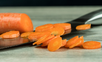 Carrot slices covering a large kitchen knife on a wooden table top, black background