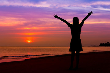Fototapeta na wymiar Silhouette of woman with hands up while standing on sea beach at