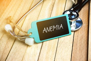 Wooden tag written with ANEMIA on wooden and stethoscope background.