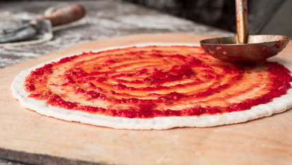 Chef hand is spreading pasteurized tomato paste onto a Pizza bas