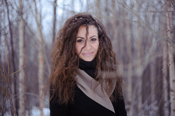 young woman with long curly hairs looking into the camera in winter snow forrest