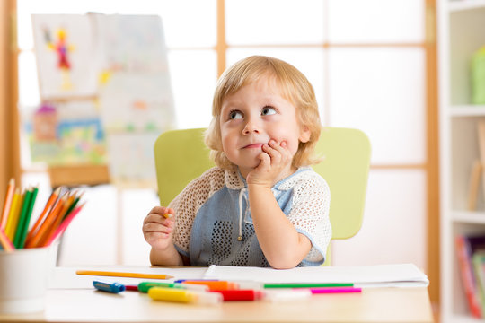 Smiling child having an idea while drawing in nursery room