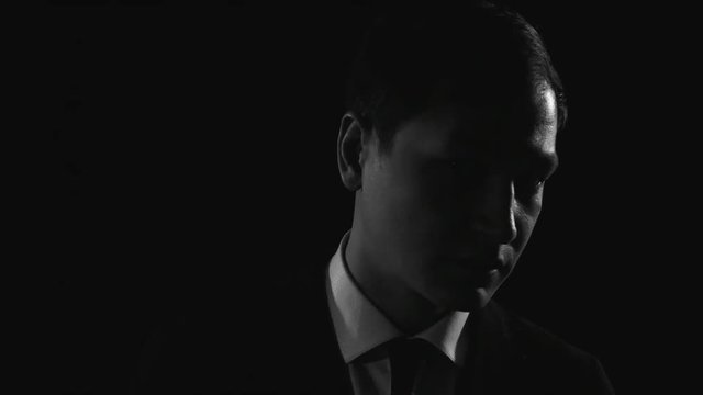 Closeup of young Asian man in formal suit turning face to camera and giving serious look in dark studio