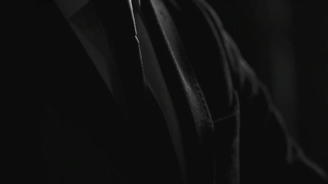 Tilt up closeup of young stylish businessman in formal suit looking at wrist watch in dark studio. Suitable for business, fashion, lifestyle, corporate portraits, luxury visuals