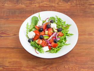 Greek salad in white dish on wooden surface