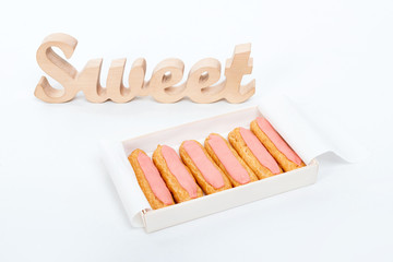 Open delivery paper box with six fresh pink cupcakes and wooden word Sweet on white background. Romantic gift. Unhealthy or dieting concept.