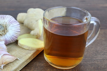 Natural treatment. Closeup cup of tea, ginger and garlic. Laid on wood with a white background.