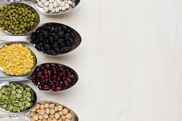 Assortment legume beans in spoons with copy space on white wood background. Top view, closeup.