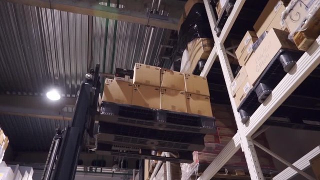 The forklift in the warehouse. A forklift raises a boxes toward the top shelf. Warehouse materials. Shelves in the warehouse.  