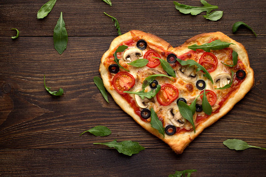 Tasty homemade pizza in heart shape with mushrooms and chicken on wooden vintage table.