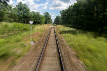 Fototapeta na wymiar Defocused railroad tracks in summer nature behind a passing train