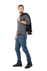 Side view of casual young man walking with jacket over shoulder looking behind. Full body length portrait isolated over white background.