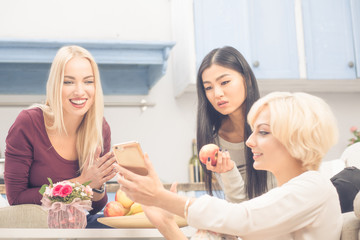Toned picture of friends girls having party at home after hard working day. Blond lady showing pictures on mobile or smart phone. Home party concept.