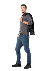 Side view of casual young man carrying jacket over shoulder looking at camera. Full body length portrait isolated over white background.