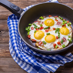 Fried eggs in pan with tomatoes and green fresh onion.