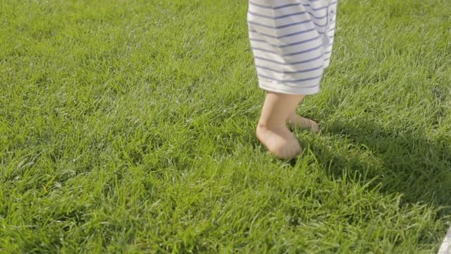 Closeup shot of cute baby boy making first steps on grass at garden