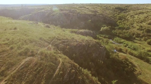 Toursits sitting on cliff near small river in rocky prairie. Shot from drone