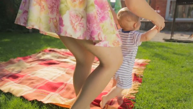 Young mother teaching making first steps her baby son on grass at backyard