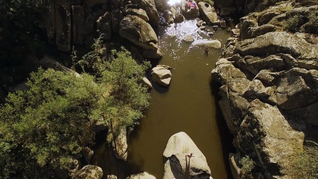 Group of people with husky dog swimming bathing in river with rocky shores and big stones. Drone shot