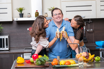 Two young women are fed bananas midle age man in the kitchen