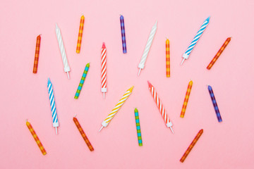 striped colorful candles for birthday party on pink background. flat lay.