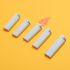 five lighters painted white with flames on yellow background.