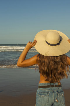 Young woman from behind, wearing beach summer hat and shorts jea