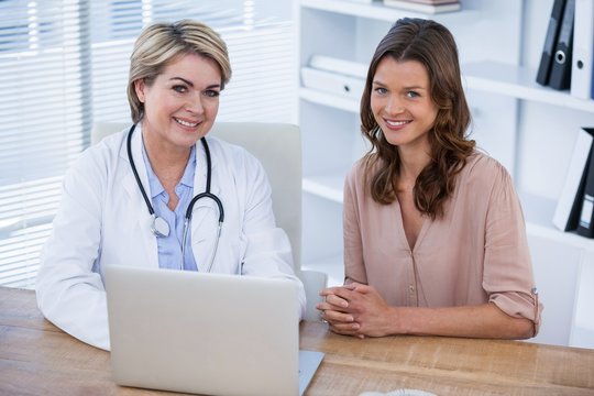 Portrait of smiling female doctor and patient sitting at desk