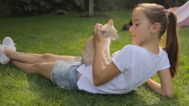 Beautiful teenage girl lying on grass with red cat on her belly