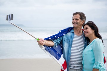 Couple wrapped in american flag taking selfie on beach