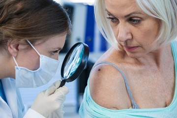 Dermatologist examining mole of female patient