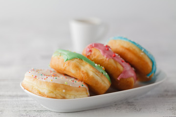 Few colorfull donuts lay on plate with cup of espresso
