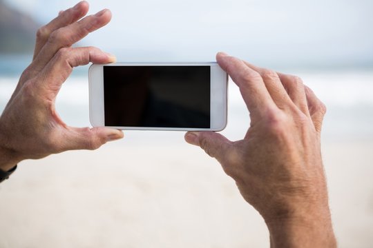 Close-up of mans hand taking picture on mobile phone on beach