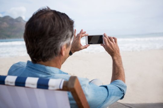 Rear view of man taking picture on mobile phone at beach