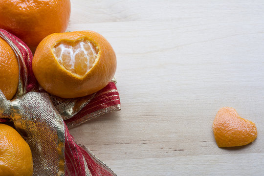 Sweet mandarin with a hole and peel in form of heart are on the wooden background