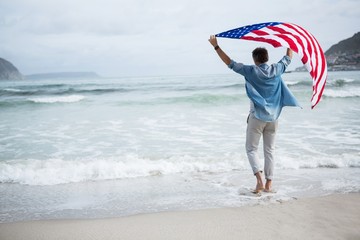 Rear view of man holding american flag on beach