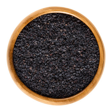 Black sesame seeds in wooden bowl. Fruits of Sesamum radiatum, also black benniseed or vegetable sesame, is eaten whole or as paste. Isolated macro food photo close up from above on white background.