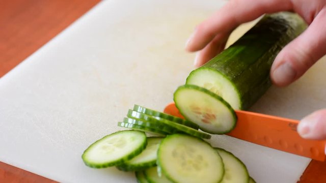 Chopping the fresh cucumber into small slices on chopping board.