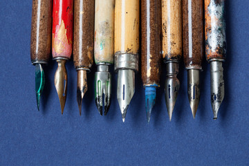 Fountain pen collection. Calligraphic accessories, aged colorful artist pens, textured blue paper...