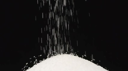 SLOW MOTION: Macro shot of falling of salt on a heap on a black background