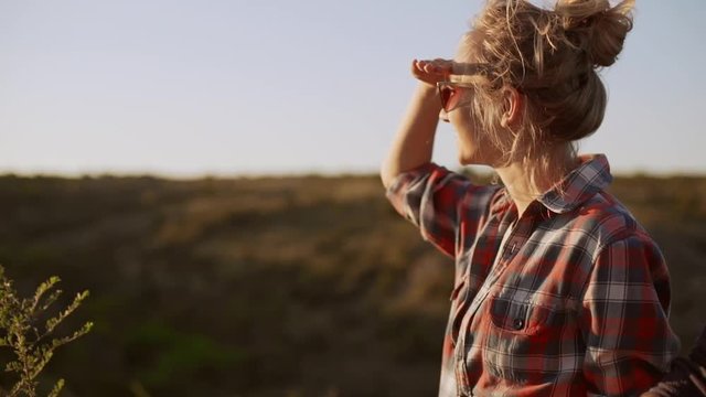 Blonde female wearing red sunglasses and plaid shirt looking forward with smile in prairie in slowmotion