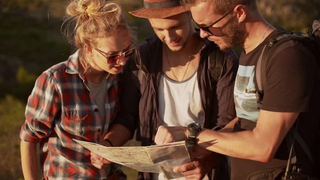Three friends looking for right way staring at map and compass outdoors in slowmotion